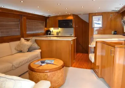 2001 Hatteras 60 Convertible “Reel Energy”: salon with cream L-shaped sofa, round burl-wood table and open galley beyond