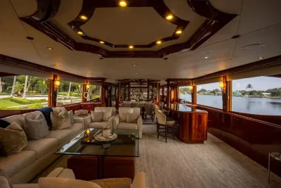 2004 Lazzara 106 Motor Yacht “Passion”: main salon with cream sofas, glass coffee table, curved wood bar and dining area beyond