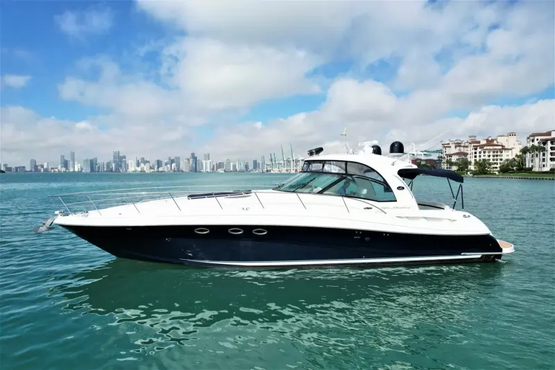 2005 Sea Ray 50 Sundancer “Nautical Dreamer”: profile of express cruiser with dark navy hull and white hardtop, guest at helm
