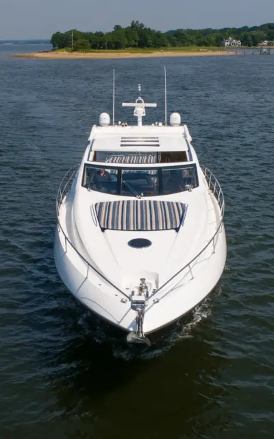 2010 Sunseeker 64 Predator “Bella”: head-on view of sport yacht with striped foredeck sunpad and guest at the helm