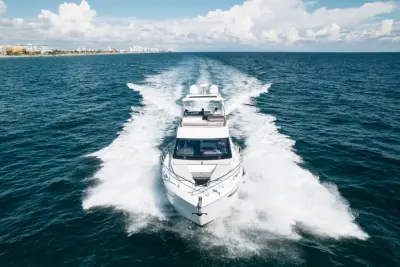 2020 Galeon 500 Fly “Livin the Dream”: head-on aerial of flybridge yacht running toward camera, wake spreading behind, guests on flybridge