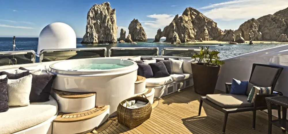The upper deck of a yacht with a spa pool and lounge seating overlooking rock formations