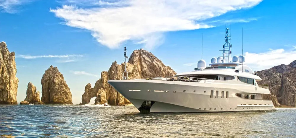 A large white motor yacht at anchor beside the rock arch at Cabo San Lucas