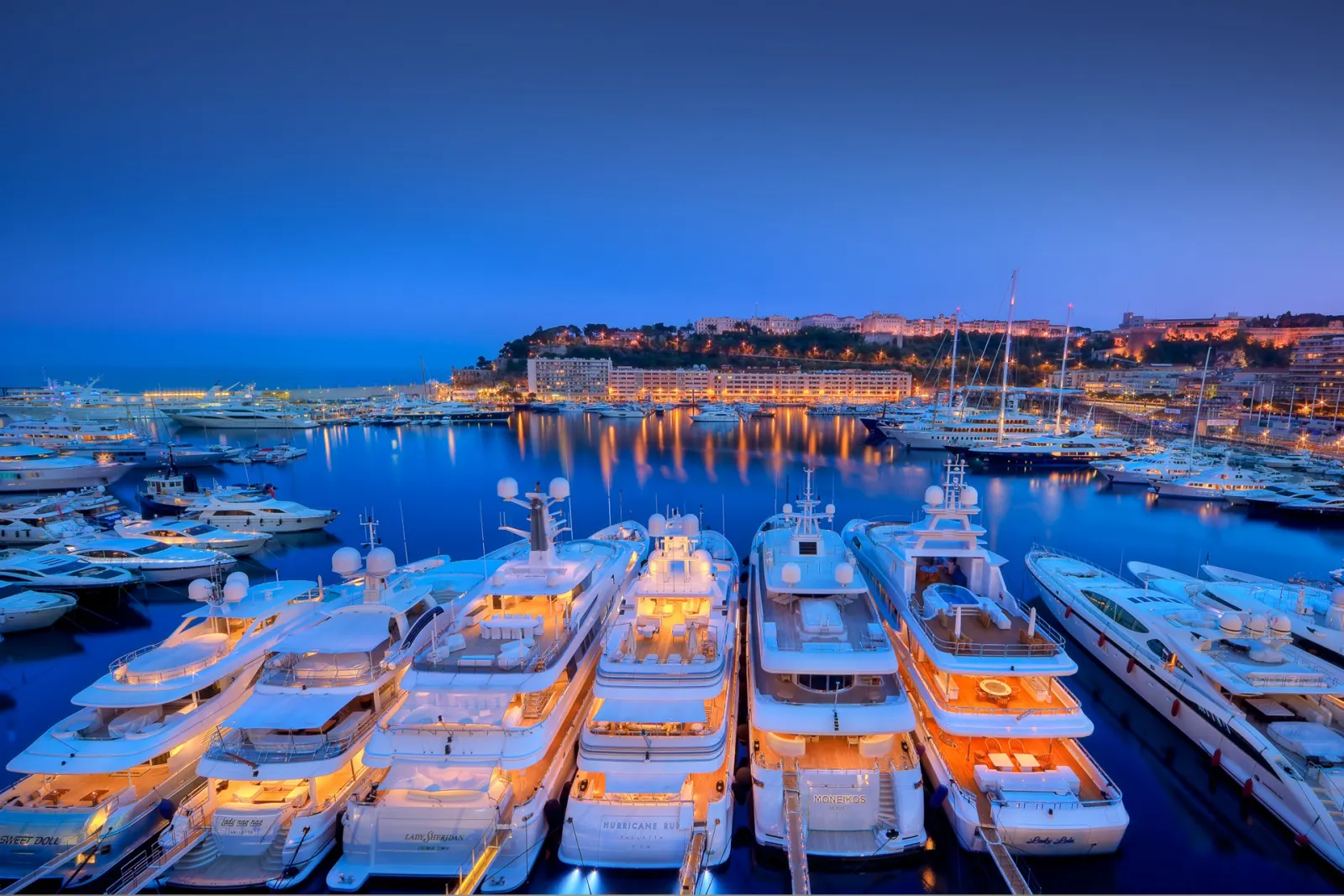 Rows of yachts berthed in a marina at dusk with lights on