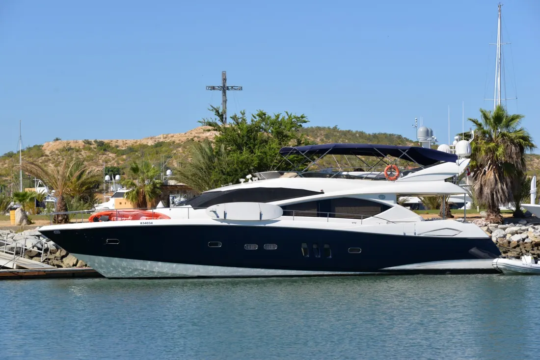 A dark-hulled motor yacht berthed at a marina with palm trees behind